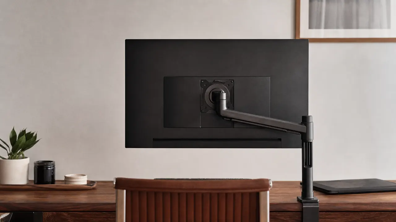 Home office desk viewed from behind showing clean cable routing through monitor arm channel