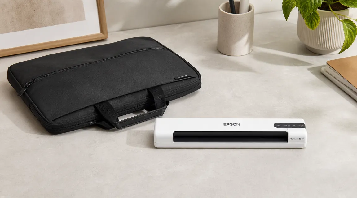 Epson ES-50 scanner lying flat next to a slim laptop bag on a neutral surface to show its compact portable size