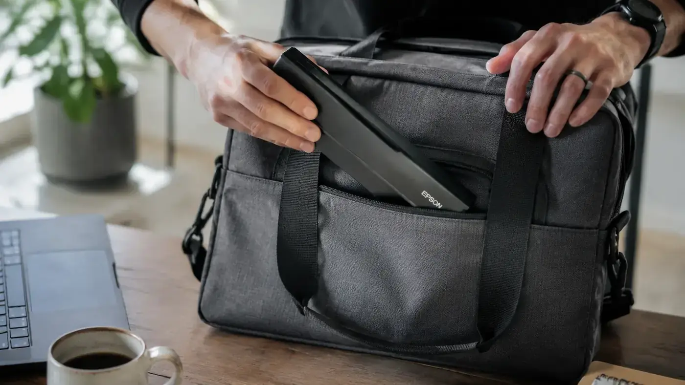 Slim portable document scanner being slipped into a laptop bag side pocket showing its compact travel form