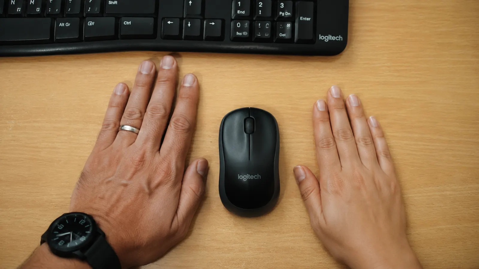 Small hand and medium hand placed side by side next to the Logitech MK270 mouse to show size fit difference